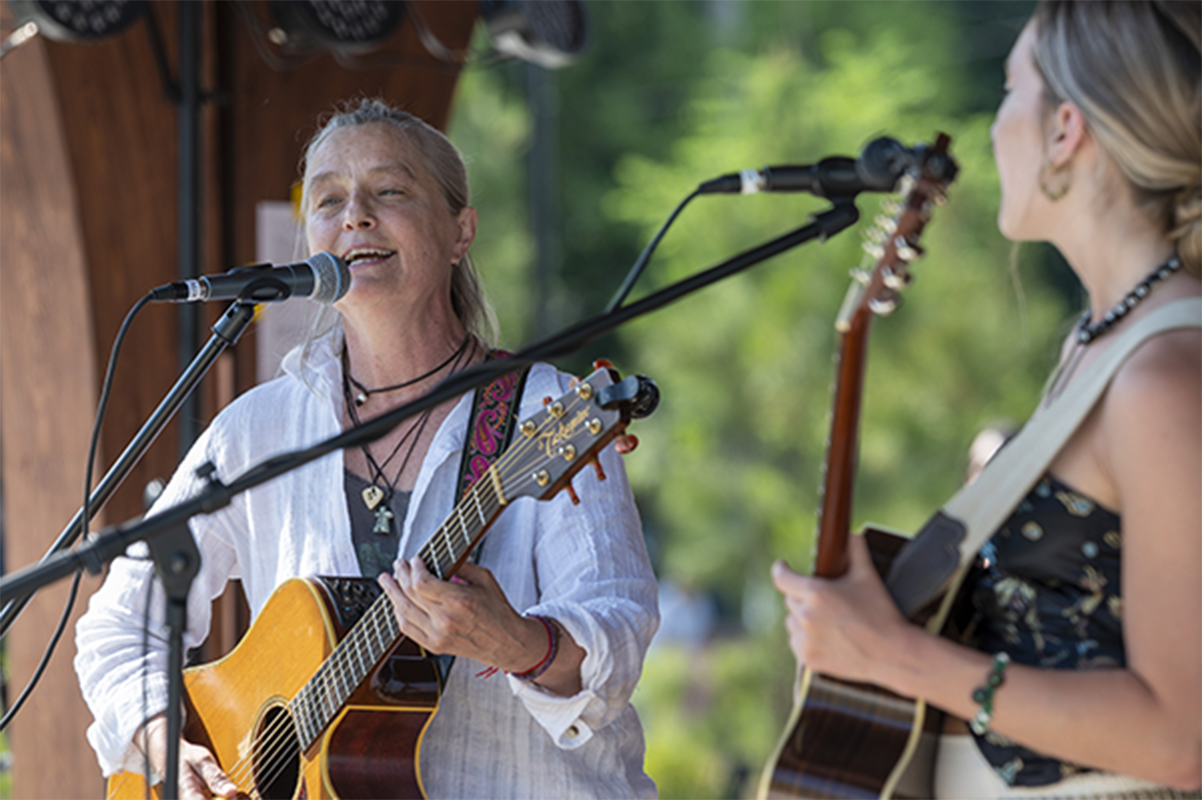 two women singing into microphones playing guitar on the Town Green stage